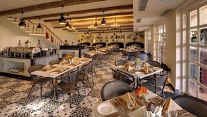 A spacious dining area with multiple tables set for guests, a staircase leading to an upper level, and a view through large windows.