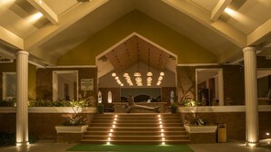 A hotel lobby with a reception desk, a staircase leading to the upper floor, and a large chandelier.
