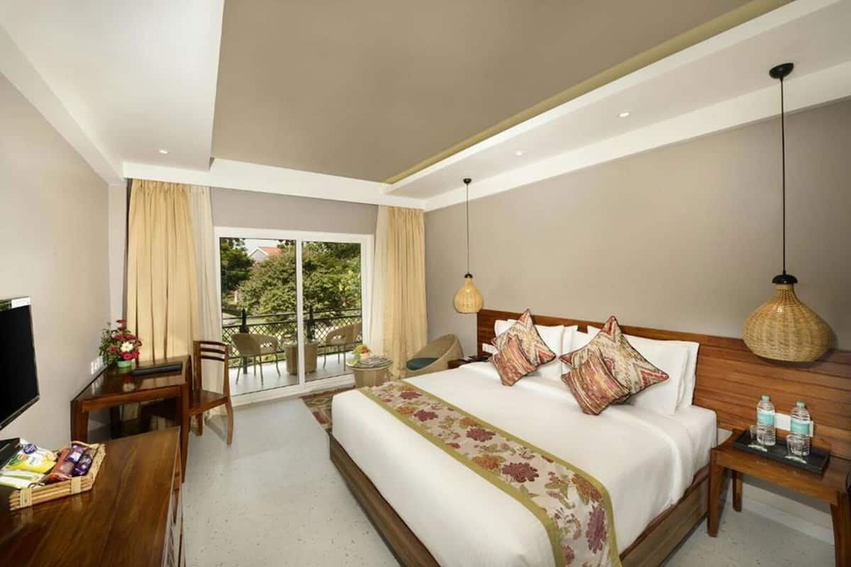 Una habitación de hotel con cama, escritorio, silla, televisor, balcón con sillas y una lámpara colgante.