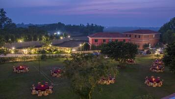 A large building with multiple dining areas, each with round tables and chairs, surrounded by a well-lit outdoor space.
