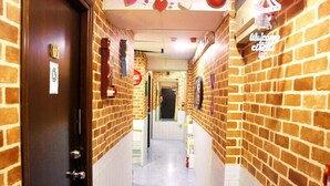 A narrow hallway with brick walls, a wooden door on the left, and a 'Welcome' sign on the right. - Ridor Guesthouse (Kowloon)