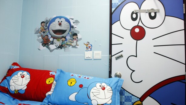 A bedroom with a blue and red bedspread featuring a cartoon character, a wall clock, and a door with a cartoon character design. - Ridor Guesthouse (Kowloon)