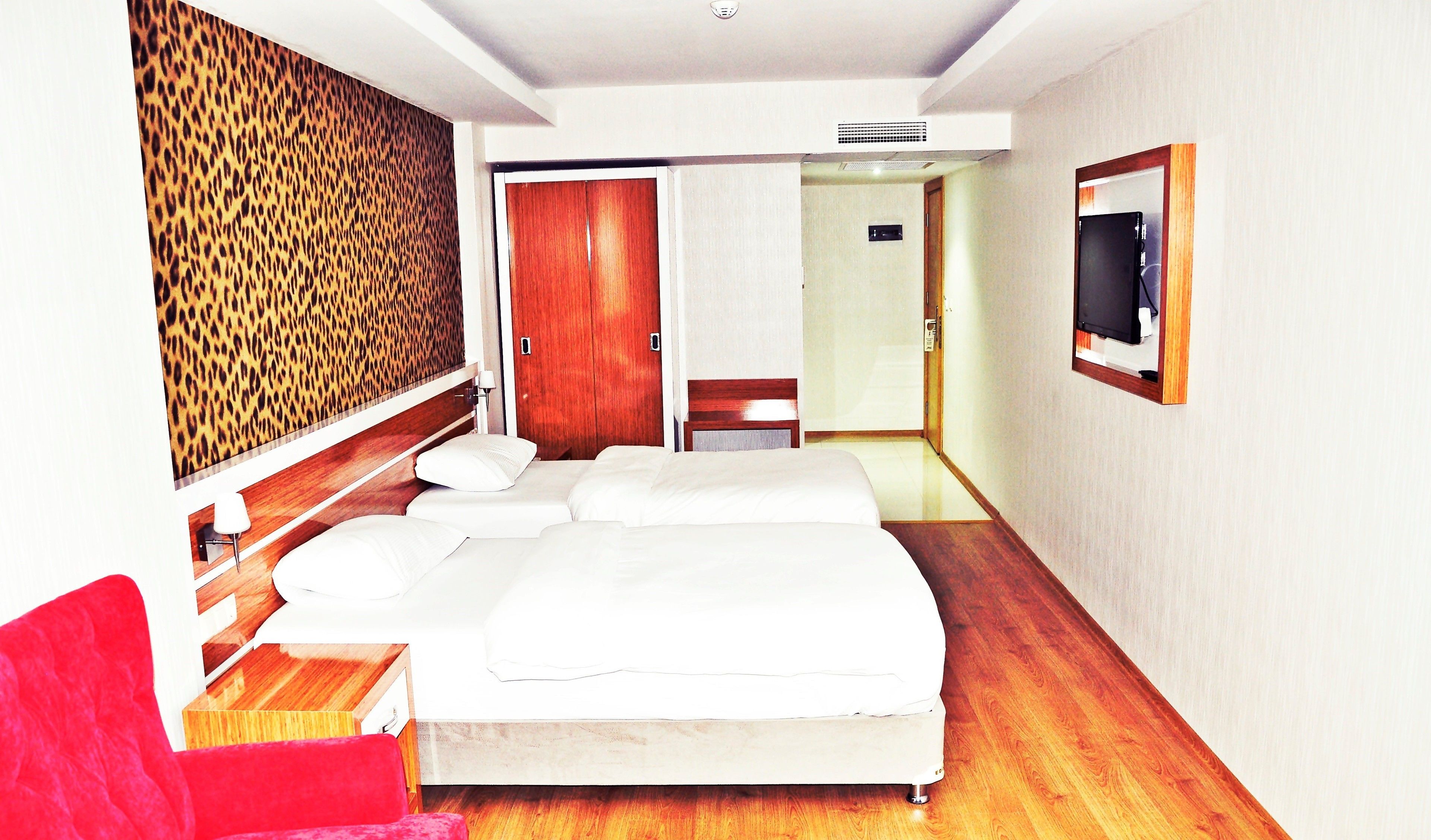 A hotel room with a bed, a red chair, a television, and a wooden floor.