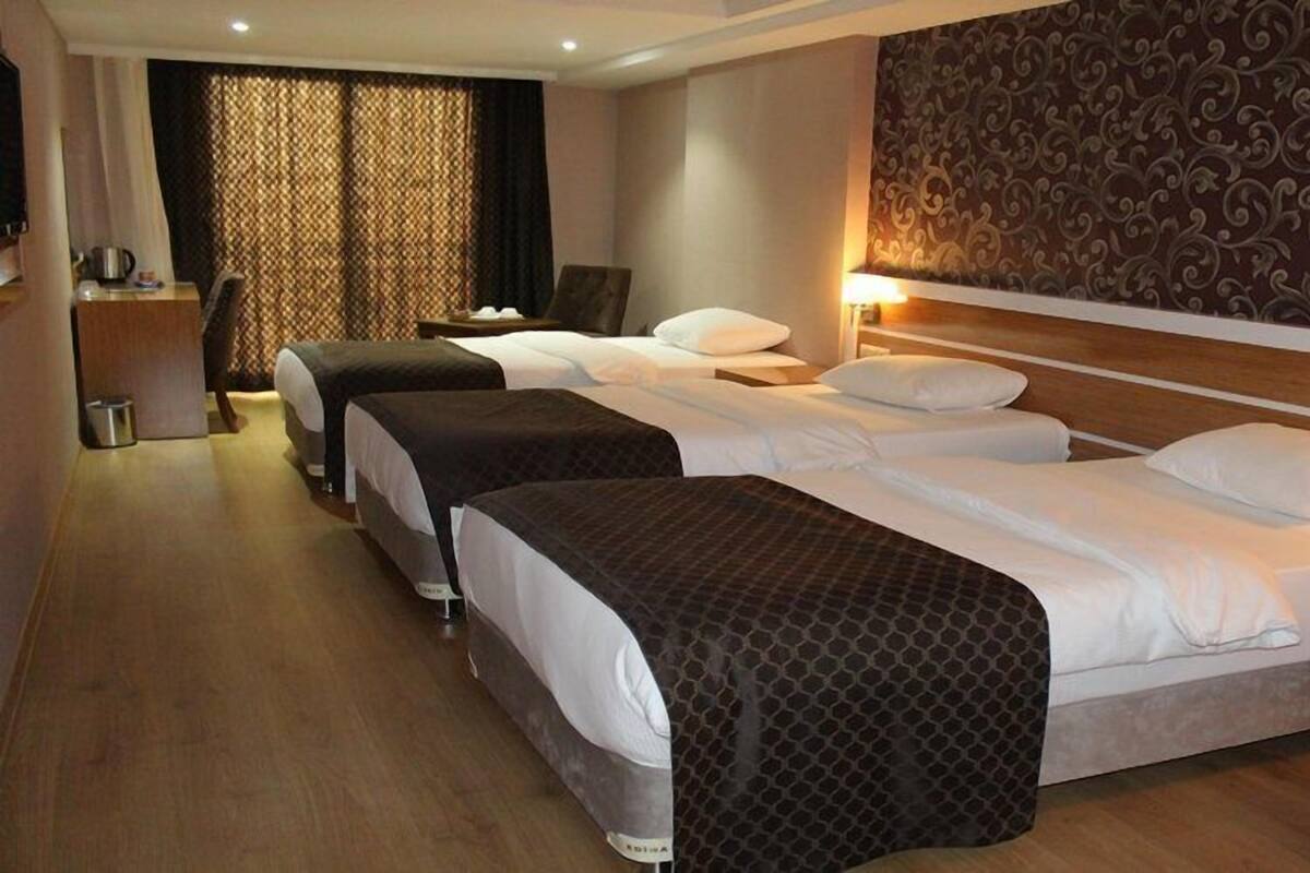 A hotel room with three beds, a desk, a chair, and a patterned wall.