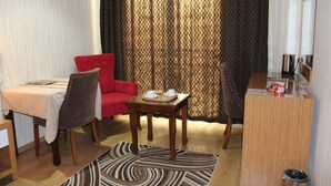 A hotel room with a dining table, two chairs, a small wooden desk, and a large window with curtains. - Bayazit Hotel (Iskenderun)