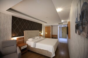 Quarto de hotel moderno com uma cama grande, mesa de cabeceira, uma cadeira e um guarda-roupa.