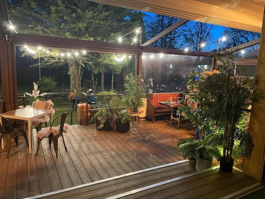 En utomhusveranda med trägolv, krukväxter och ljusslingor.