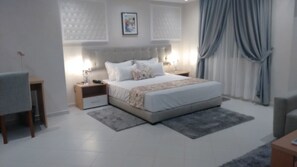 A modern bedroom with a large bed, bedside tables, a desk, and a chair.