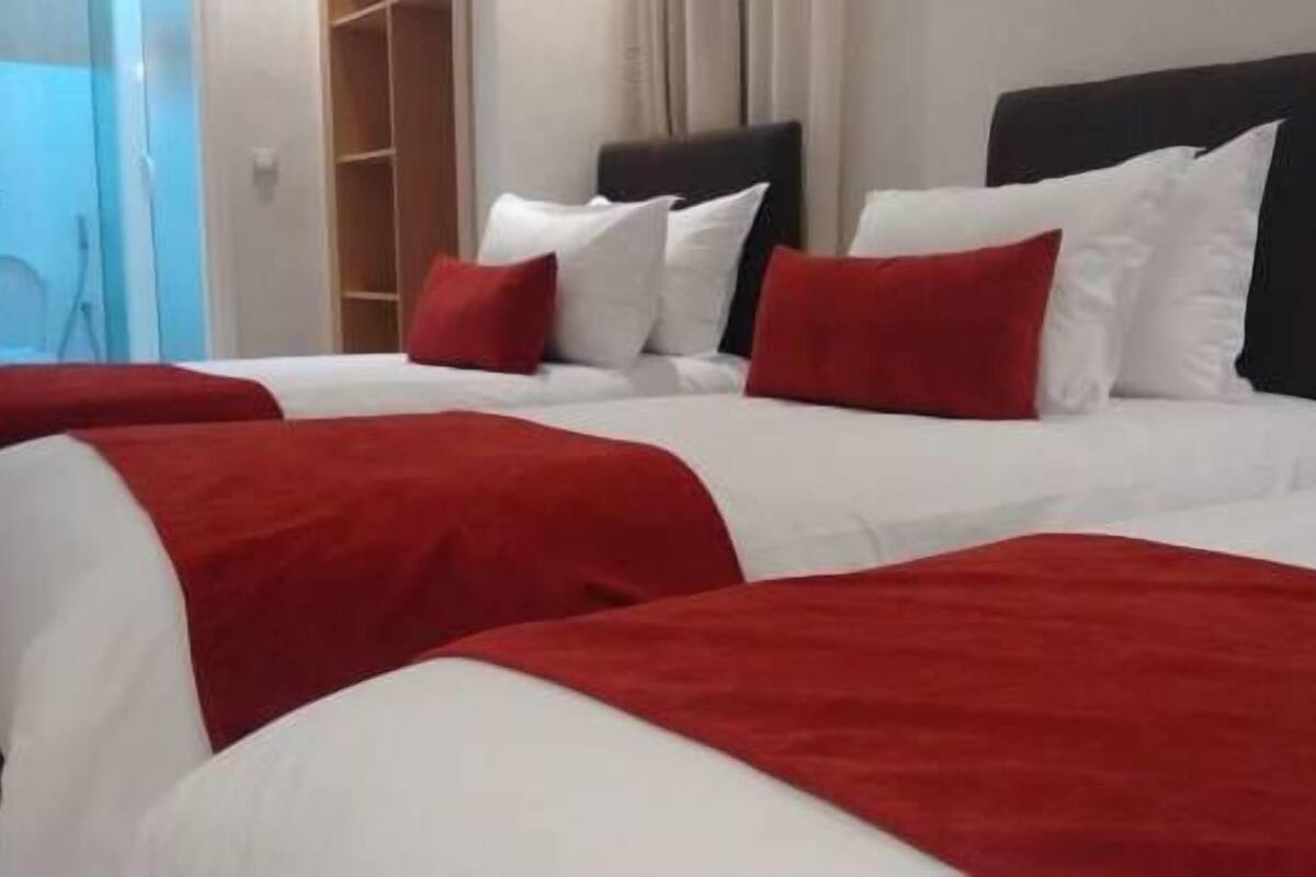 A hotel room with two beds, each with white bedding and red accents.