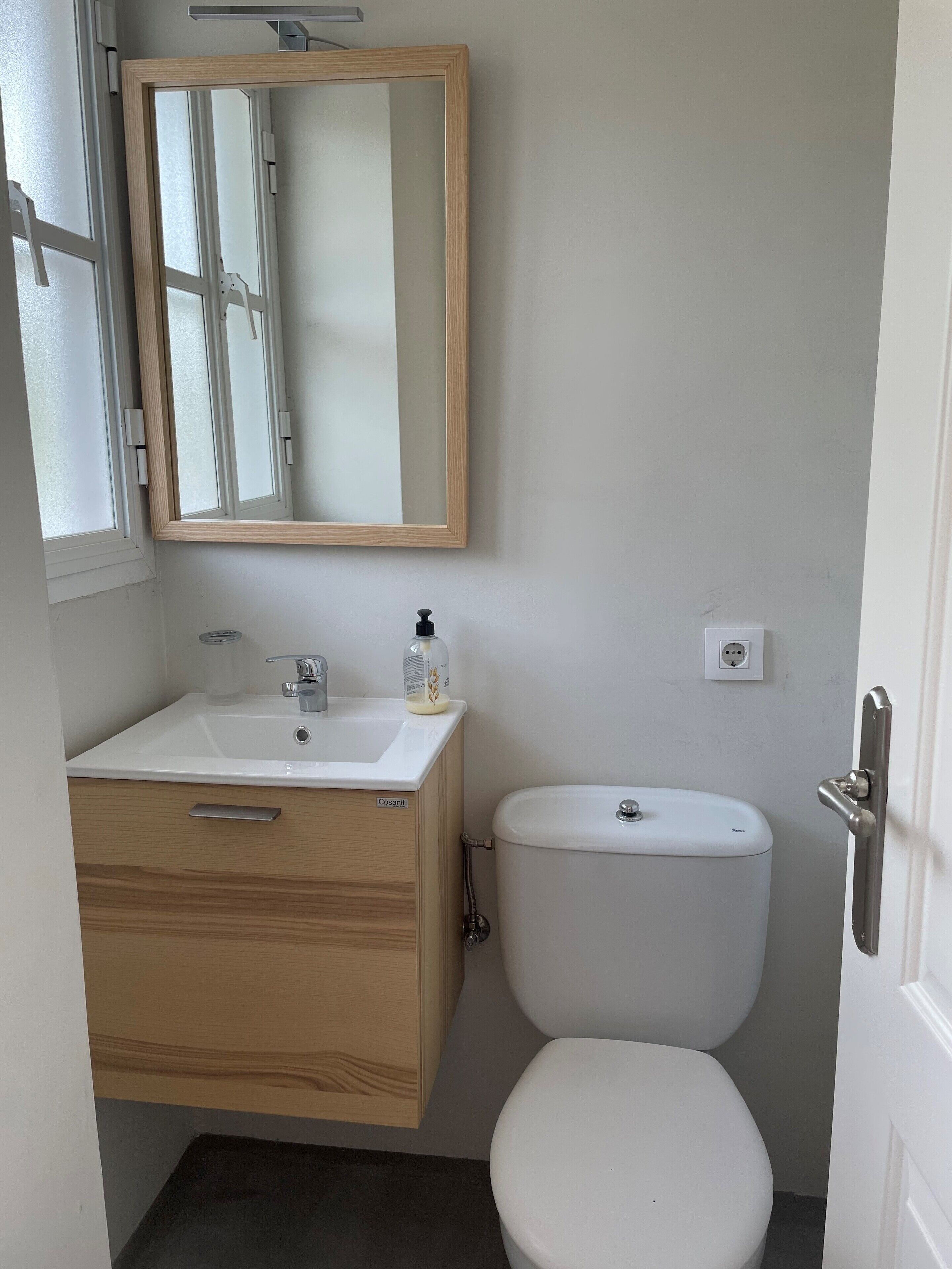 Ein kleines Badezimmer mit einem Holzbadezimmermöbel, einem weißen Waschbecken, einem Spiegel und einer weißen Toilette.
