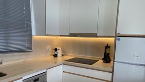Una cocina compacta con armarios blancos, lavavajillas integrado, cafetera y refrigerador.