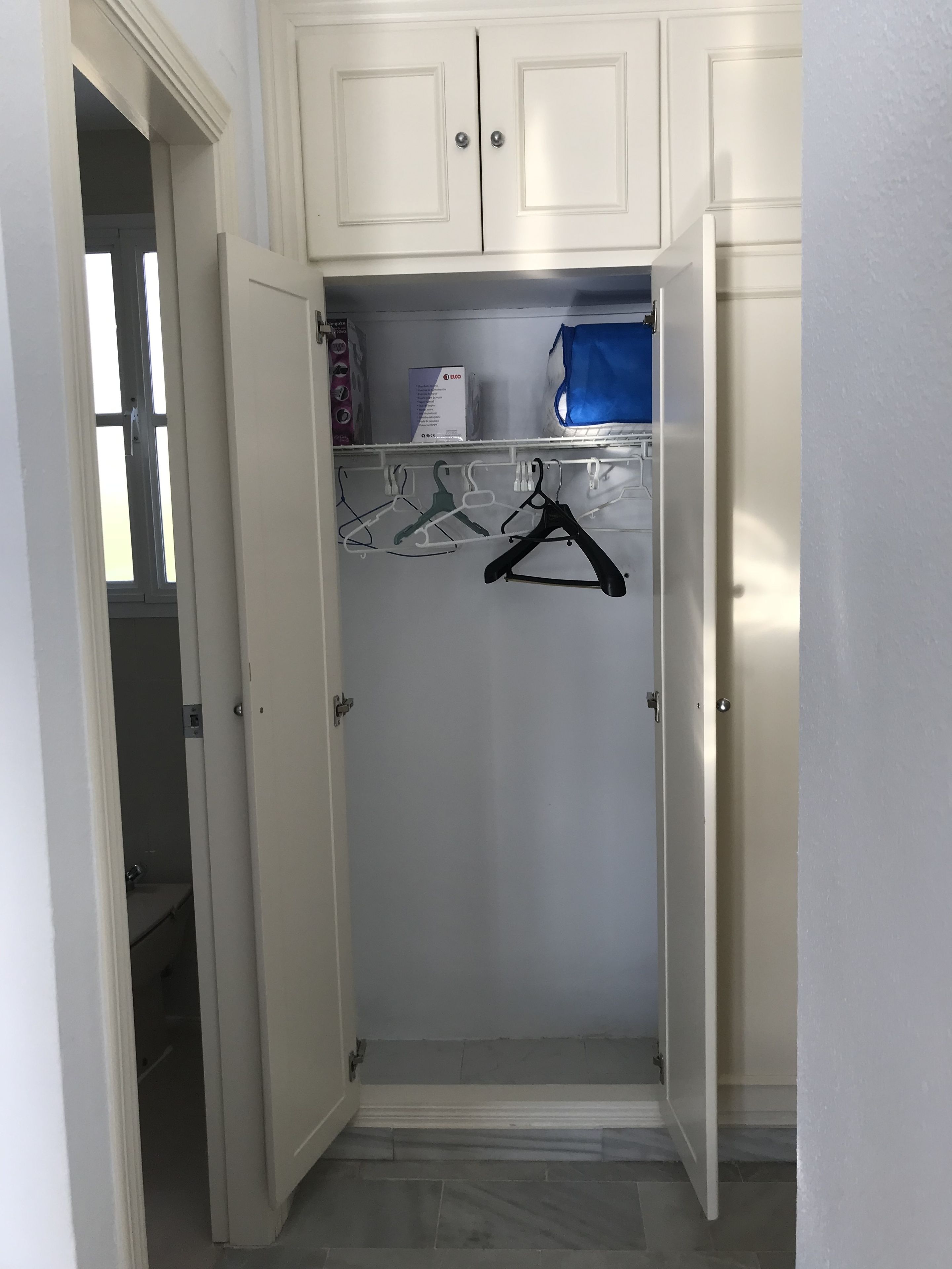 A walk-in closet with a door, a hanging rack, and a blue storage bin.