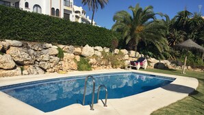 Una piscina con un muro de piedra y palmeras al fondo.