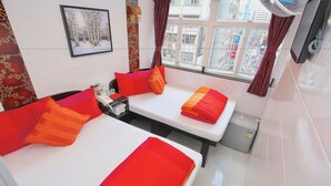 A hotel room with two beds, red and orange bedding, a small table with a phone, a nightstand, a window with curtains, and a wall-mounted TV. - D Red Loft (Kowloon)