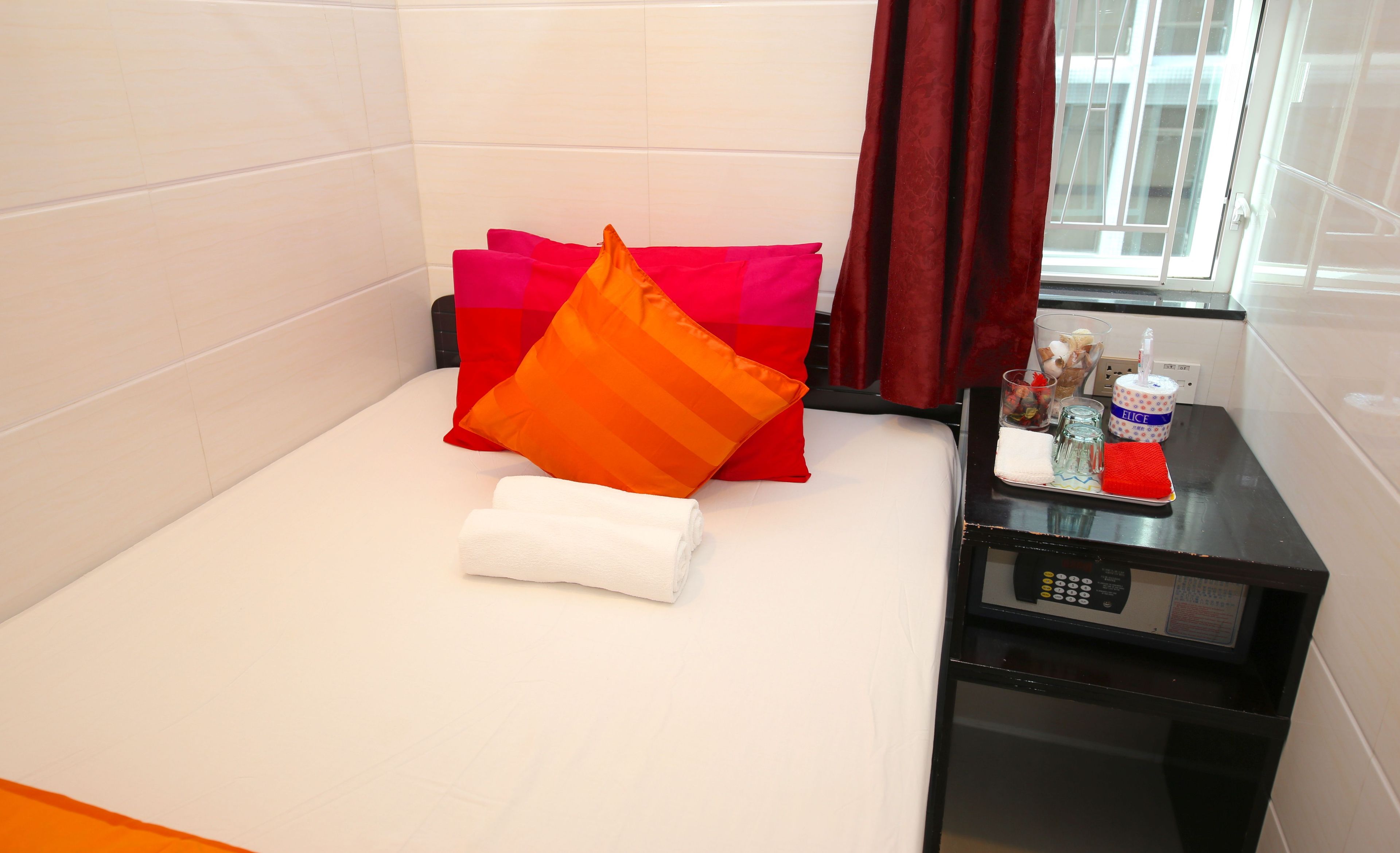 Habitación de hotel con cama, almohadas, una toalla doblada con esmero, una mesita de noche con microondas y una ventana con cortinas.