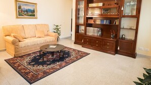 Una sala de estar con un sofá color crema, una mesa de centro, una estantería de madera y un cuadro enmarcado en la pared.