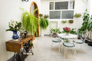 A cozy dining area with a wooden table and white chairs, surrounded by potted plants and a sewing machine. - Casa Nonna Rosa (Ragusa)