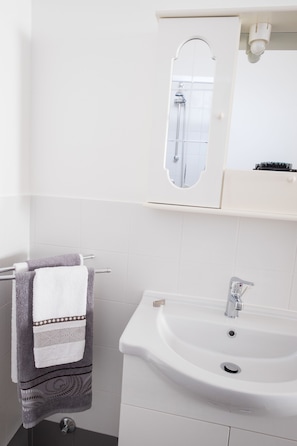 Un baño con lavamanos blanco, toallero con toalla, espejo y zona de ducha.