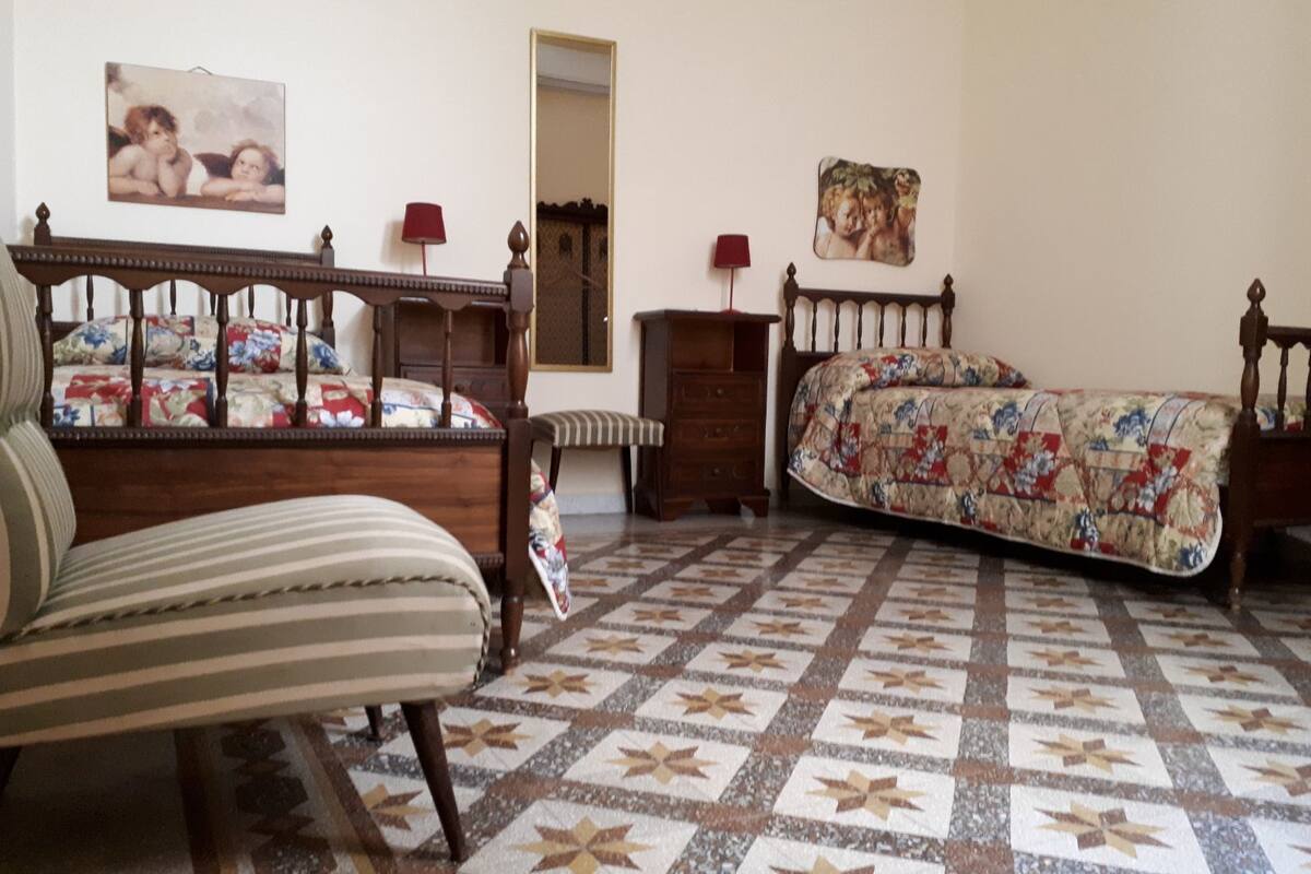Un dormitorio con una cama y una silla de madera, un aparador y un espejo.
