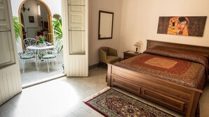 Un dormitorio con cama de madera, un espejo grande, un cuadro, una mesita con lámpara y vistas a un comedor con mesa y sillas.