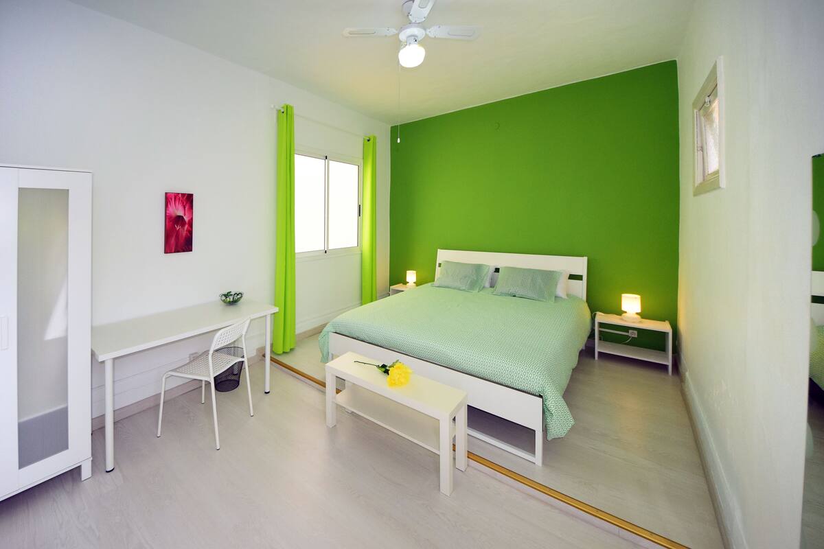 Une chambre à coucher comprenant un lit, un bureau, une chaise, un banc, une table de chevet et une fenêtre.
