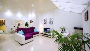 Ein modernes Wohnzimmer mit einem violetten Ecksofa, einem Flachbildfernseher und einem weißen Couchtisch.