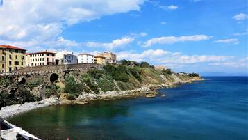 A coastal town with a historic stone bridge, clear blue sea, and buildings with red roofs.