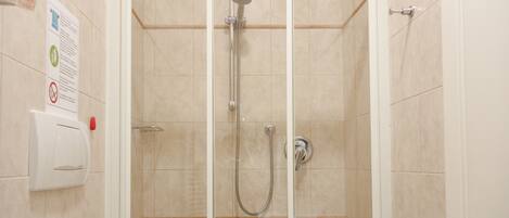 Un box de ducha con paredes de vidrio, cabezal de ducha de mano y grifo instalado en la pared.