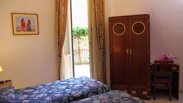 Un dormitorio con dos camas, un armario de madera, un escritorio con silla y una puerta que da a un balcón.