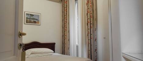 A bedroom with a bed, an air conditioner, a door, and a window with curtains.