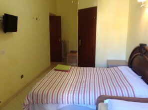 Un dormitorio con cama, mesita de noche, televisor montado en la pared y una puerta que da a otra habitación.