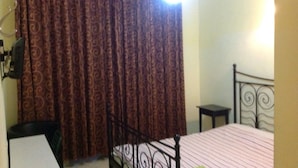 A bedroom with a bed, a desk, a chair, a curtain, and an air conditioning unit.