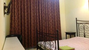 A bedroom with a bed, a bedside table, a chair, a curtain, and an air conditioning unit.