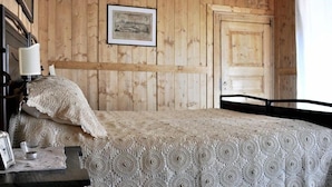 Une chambre avec des murs recouverts de panneaux de bois, un lit avec une couvre-lit à motifs, une table de chevet avec une lampe et un tableau encadré au mur.