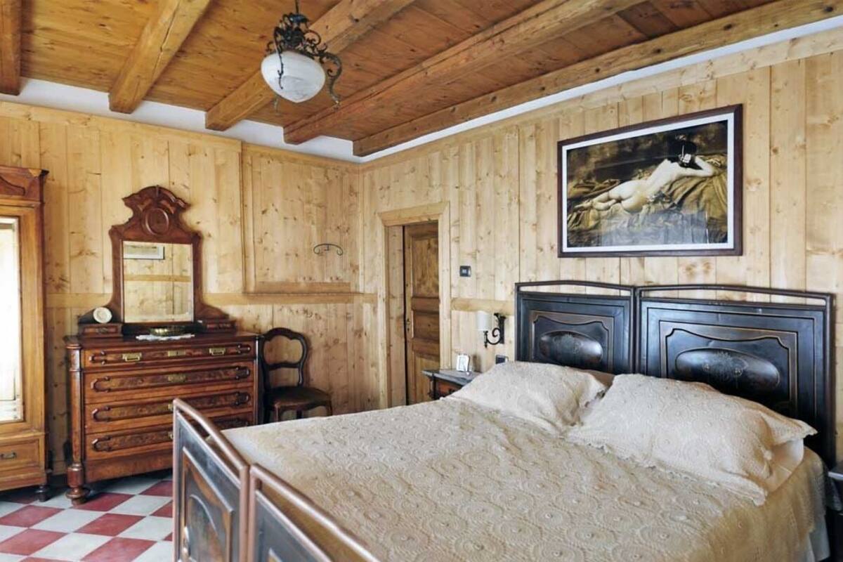 A wooden-paneled room with a bed, dresser, and a painting on the wall.