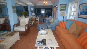 Uma sala de estar com sofá, poltronas, mesa de jantar e lustre.