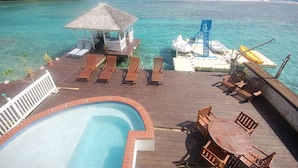 Um deck de madeira com piscina, espreguiçadeiras e um pequeno gazebo com vista para águas turquesa.
