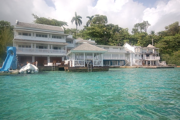 A beachfront property with multiple buildings, including a large house with a balcony and a smaller structure with a covered patio.