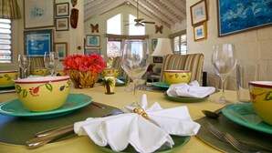 A dining table set with green plates, yellow bowls, and white napkins. There are wine glasses and a vase with red flowers.