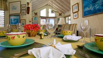 A dining table set with green plates, yellow bowls, and white napkins. There are wine glasses and a vase with red flowers.