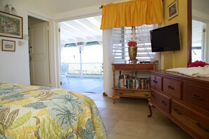 A bedroom with a bed, a wooden dresser, a TV, and a bookshelf. - Windjammer, 4BR by Jamaican Treasures (Boscobel)