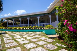 A covered porch with a checkered stone pathway leading to a building with a white railing and columns. - Windjammer, 4BR by Jamaican Treasures (Boscobel)