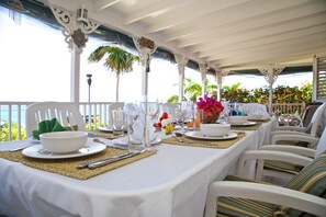 A covered outdoor dining area with white tables set for a meal, surrounded by white chairs with striped cushions. - Windjammer, 4BR by Jamaican Treasures (Boscobel)