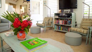 A living room with a sofa, chairs, a coffee table with a book and a vase of flowers, a bookshelf, and a television.