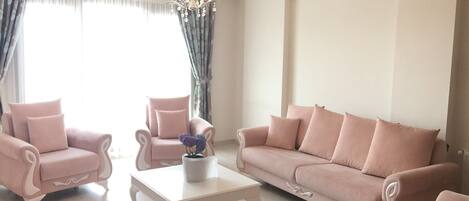 A living room with a sofa, two armchairs, a coffee table, and a red ottoman.