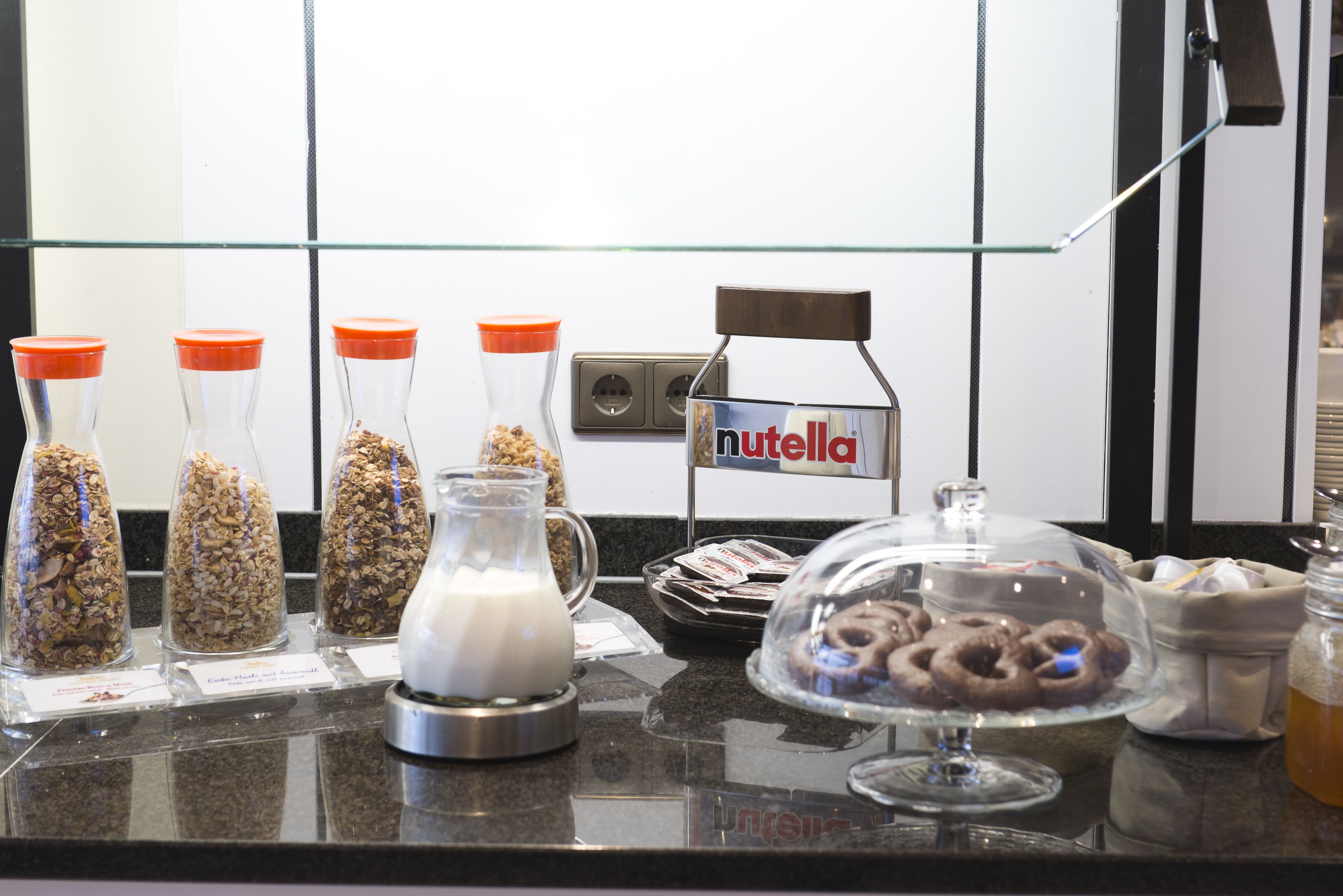 A breakfast bar with various food items, including granola, milk, and pastries, with a Nutella sign above.