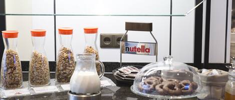 A breakfast bar with various food items, including granola, milk, and pastries, with a Nutella sign above.
