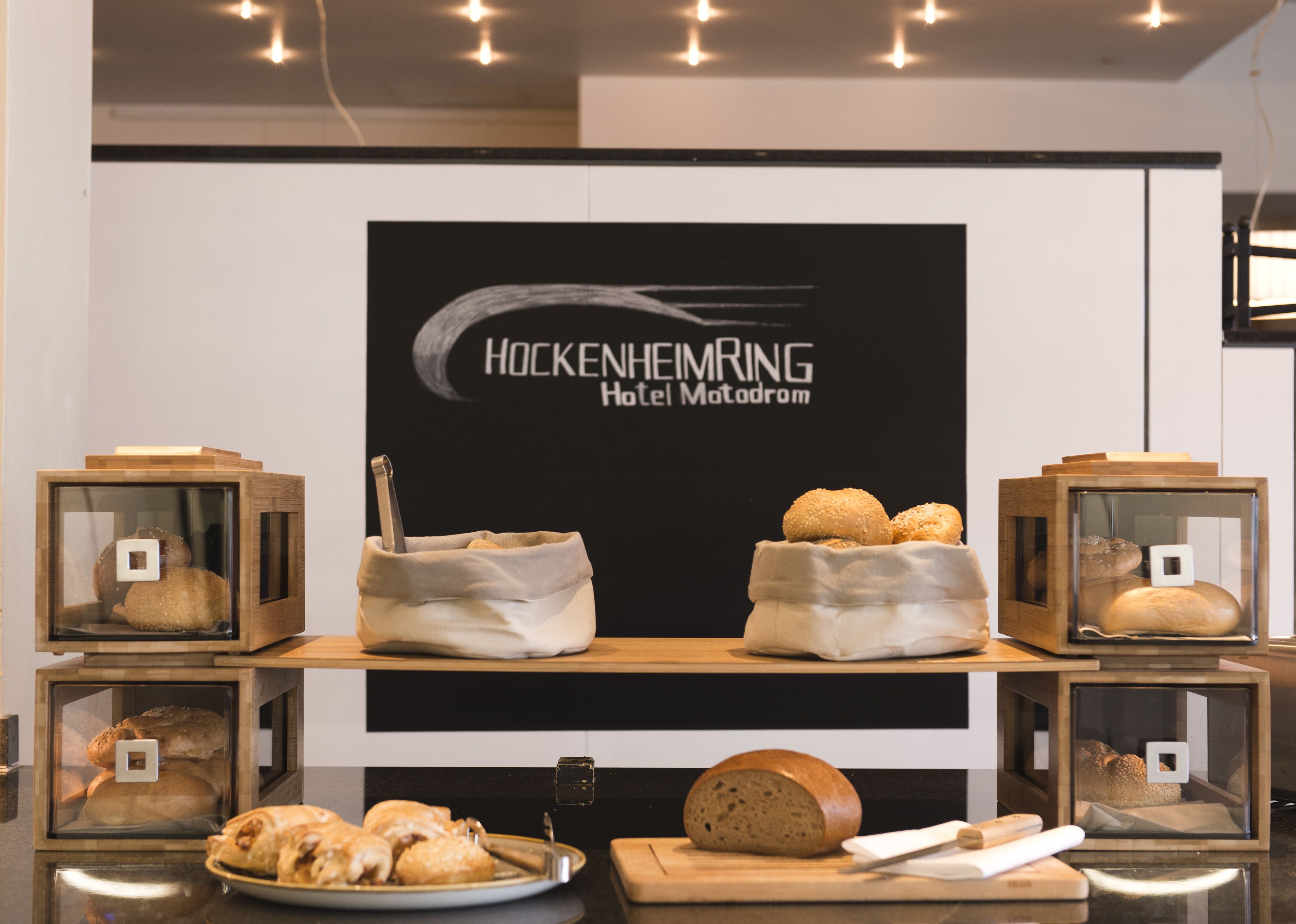 A display of bread and pastries in wooden boxes, with a sign reading "Hockenheimring Hotel Matadrom" in the background.