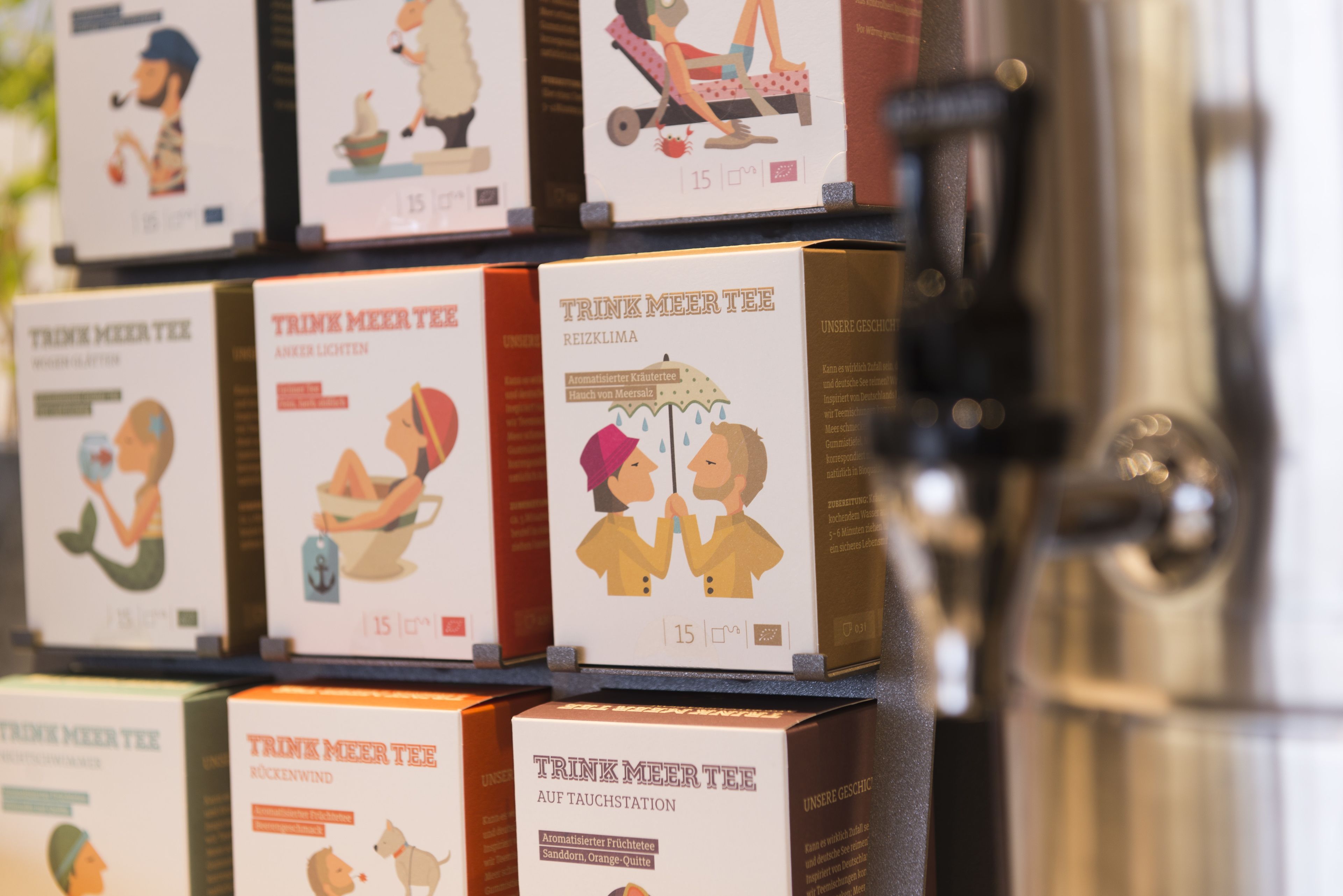 Une présentation de boîtes de TRINK MEER TEE, illustrées avec des images de personnes et de chiens, chacune étant étiquetée avec un prix de 15 €.