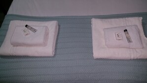 Two neatly folded towels with a bottle of lotion on each, placed on a bed with a textured grey blanket. - The Oxford House (Oxford)